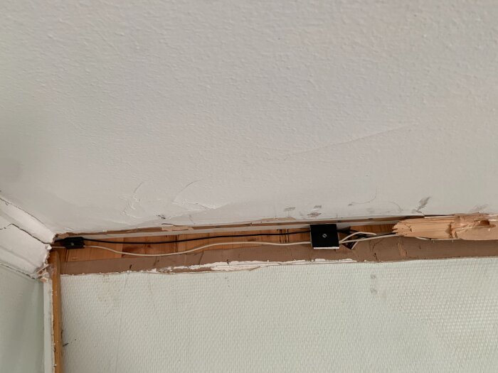 Detalj av ett renoveringsprojekt där del av taket och väggen är exponerade med synliga kablar; tyder på arbete med el och gips.