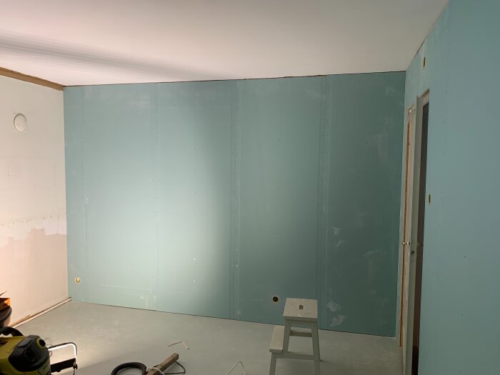 Rum under renovering med monterade lättviktsgipsskivor på väggarna, en stege och verktyg syns på golvet.