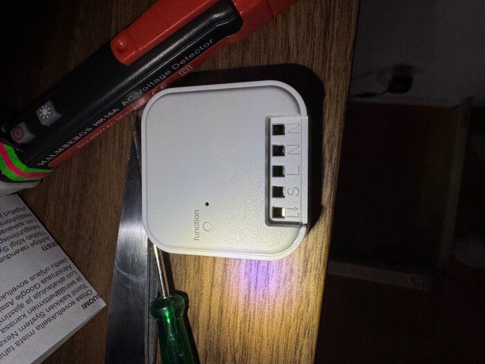 Nexa Dimmersändare på träbord med skruvmejsel och spänningsdetektor; terminaler märkta N, L, S syns.