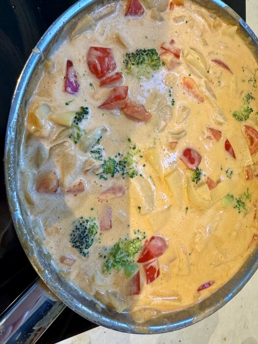 En gryta med thailändsk curry innehållande broccoli, tomater och andra grönsaker i en krämig sås.