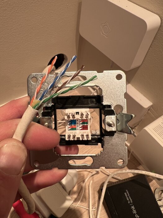Närbild på en hand som håller ett Ethernet-vägguttag med flera exponerade färgade kablar i ett kabelutrymme.
