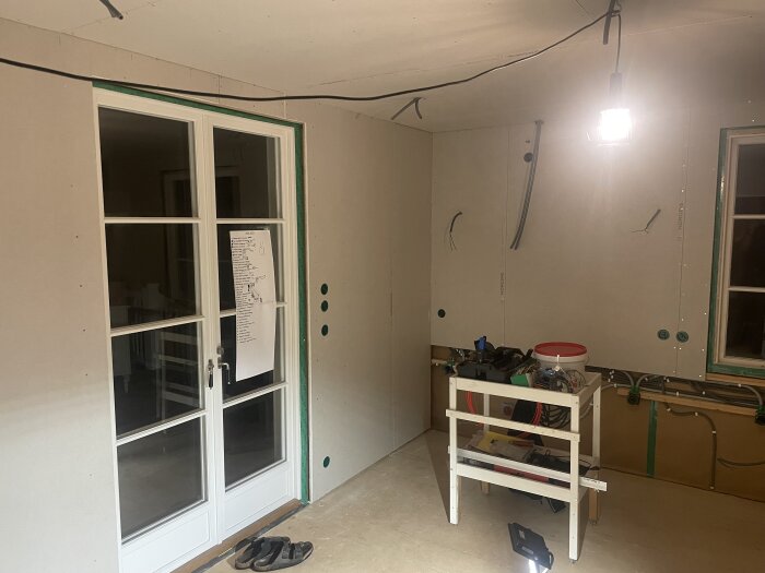 Orenoverat kök under arbete med synliga verktyg på bänk, sladdar på vägg och hängande lampa i taket.