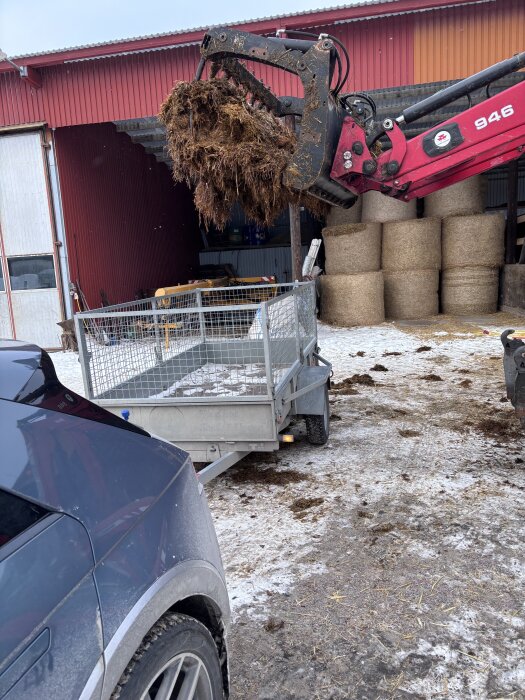 Traktor från gård lastar gödsel på släpkärra vid en lada.