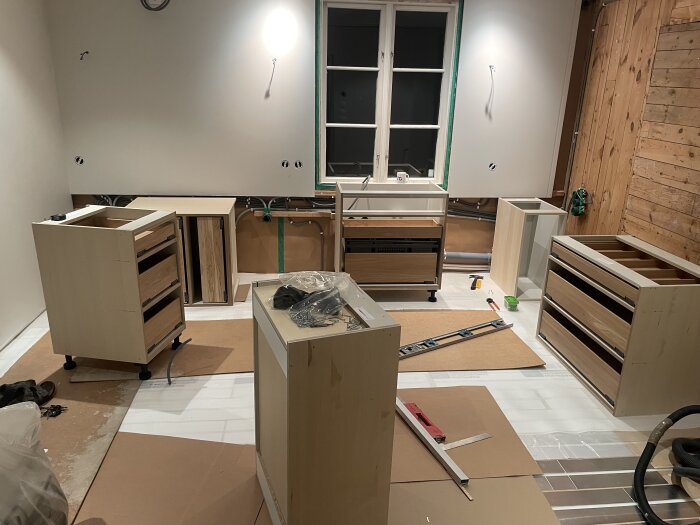 Pågående köksrenovering med monterade skåpstommar, verktyg och material utspridda i ett rum, delvis installerade hyllplan under arbete.