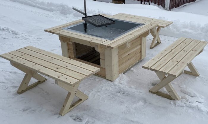 Grillplats med träbänkar och grillgaller, placerad på snötäckt mark.