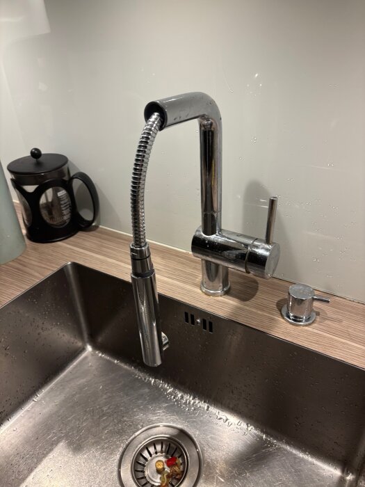 Köksblandare med avtagbar duschslang över en diskho av rostfritt stål, med vattenstänk runt om.