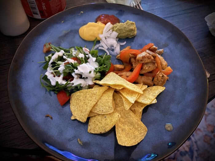 Tallrik med taco kyckling, paprika, picklad lök, ostsås, salsa, guacamole, vitlöksdressing, grönsaker och tortillachips.