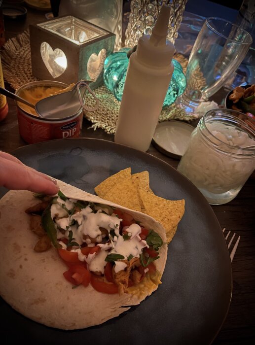 Tortilla med kyckling, paprika, grönsaker, vitlöksdressing och tortillachips på en tallrik, omgiven av dip och picklad gullök.
