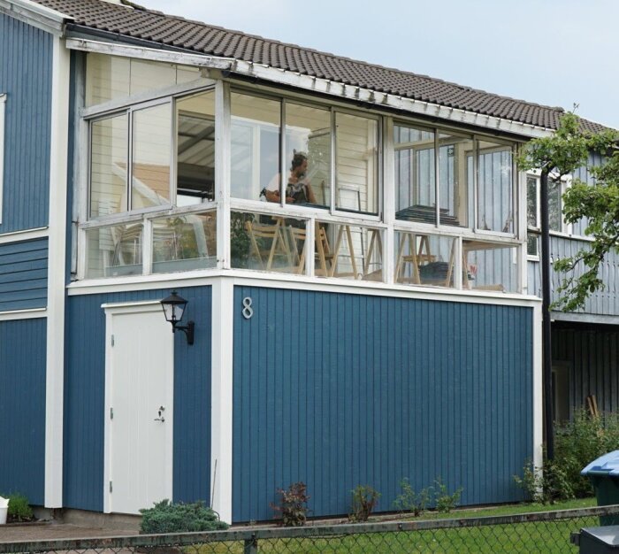 Blått hus med glasveranda och vit dörr, där panelen når hela vägen upp. Plåt ovanför fasaden syns också.