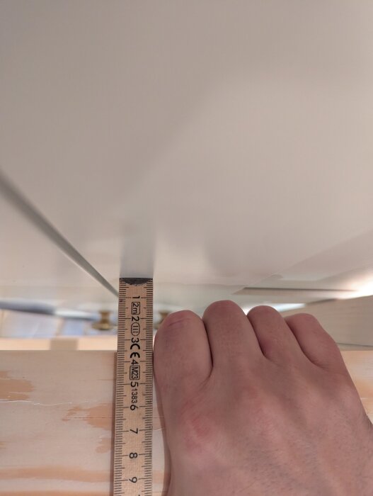 Hand mäter avståndet till stege med linjal, visar utrymme mellan handtag och steg.