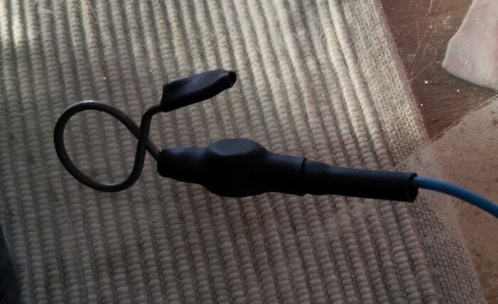 Svart kabel med ringformad kontakt för elstängsel, ligger på en matta. En kontakt fäst vid en kabel som leder till elaggregatet.