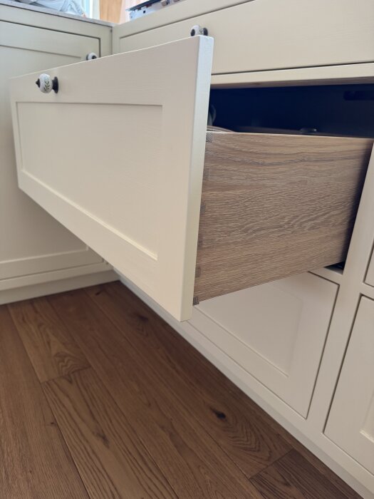 Öppen kökslåda med vit front och träfärgad insida, del av pågående köksrenovering.