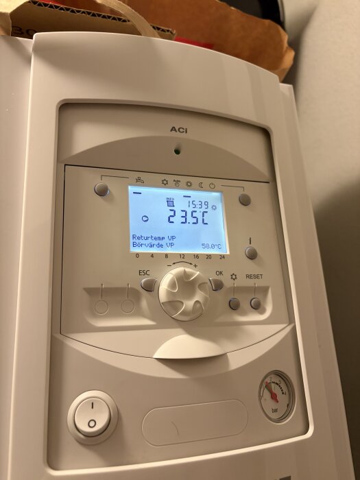 Kontrollpanel på en värmepump med digital display som visar temperatur 23,5°C och övriga inställningar, omgiven av vridknappar och mätare.