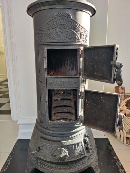 Morsø kamin med öppna dörrar, modell 116A eller 117A från ca 1912, detaljerad dekor och insyn i eldstaden. Eldning med torkad ved.