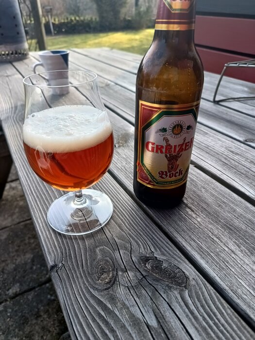 Flaska och glas med öl på träbord utomhus.
