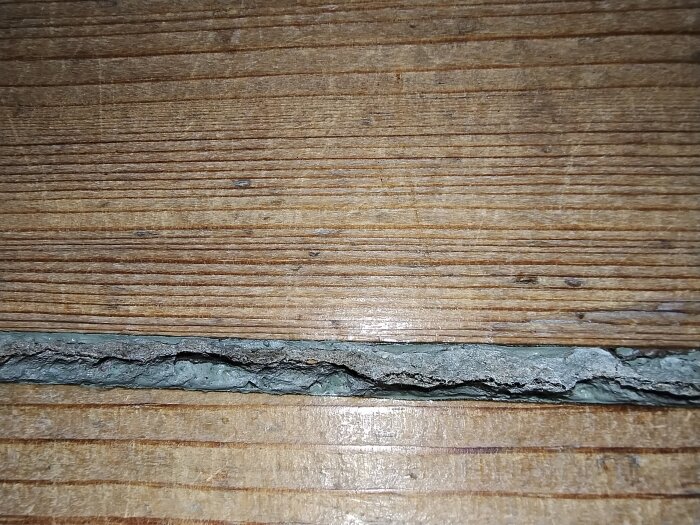 Spricka i trätrappa med grått, hårt material fyllande springan, potentiellt en gammal kakelfog som kan innehålla asbest enligt inlägg.