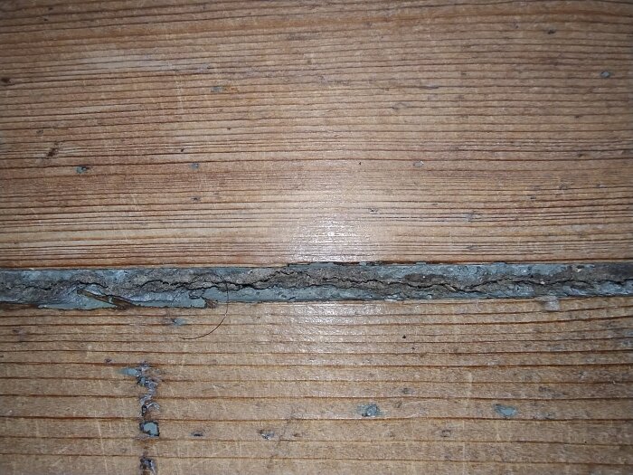 Springa mellan träplankor fylld med grått, hårt material. Möjlig fogmassa i en trappa i ett 1920-tals hus.