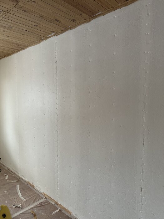 En målad fiberplankpanel med skarvar synliga, förberedd för spackling och tapetsering. Tak i trä och golv täckt med papper och tejp.