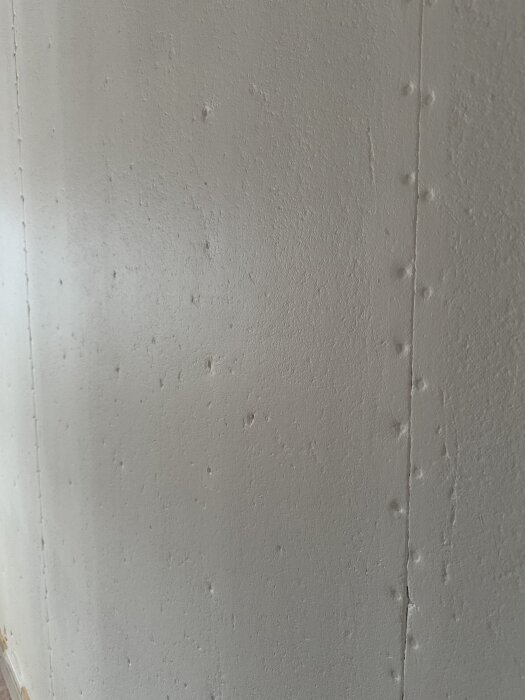 Slipad fiberplankpanel målad med spärrfärg, visar skarv och hål, i förberedelse för renovering och tapetsering.