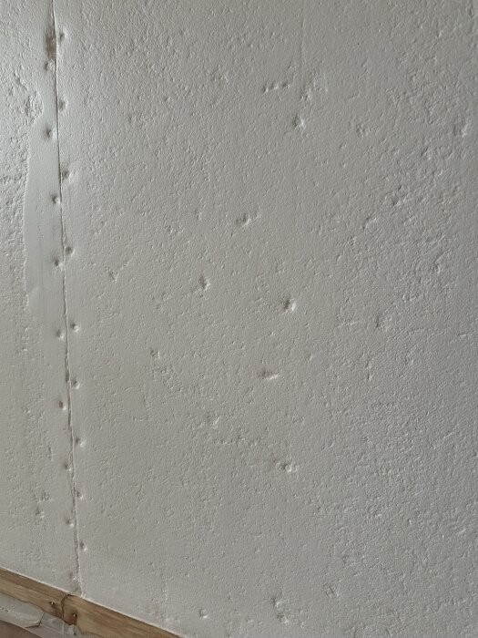 Oregelbunden yta av slipad fiberplankpanel med synliga skarvar och strukturer, förberedd för vidare renovering med spackel och eventuell tapet.