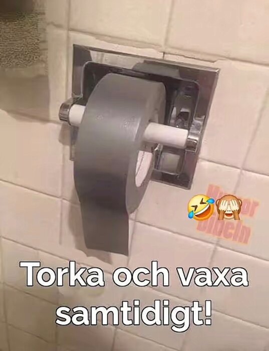 Toalettpappershållare med en rulle silvertejp monterad. Text: "Torka och vaxa samtidigt!" och emojis av skrattande och apa som håller för ögonen.