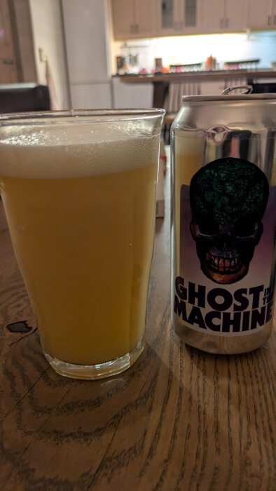 En ölglas med ljus öl och en burk märkt "Ghost in the Machine" ovanpå ett träbord i köksmiljö.