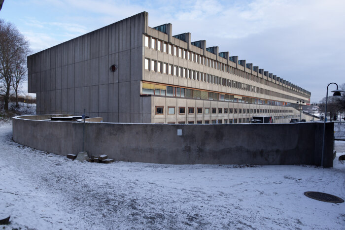 Modernistisk betongbyggnad designad av Peter Celsing med snöbelagd mark och träd i bakgrunden.