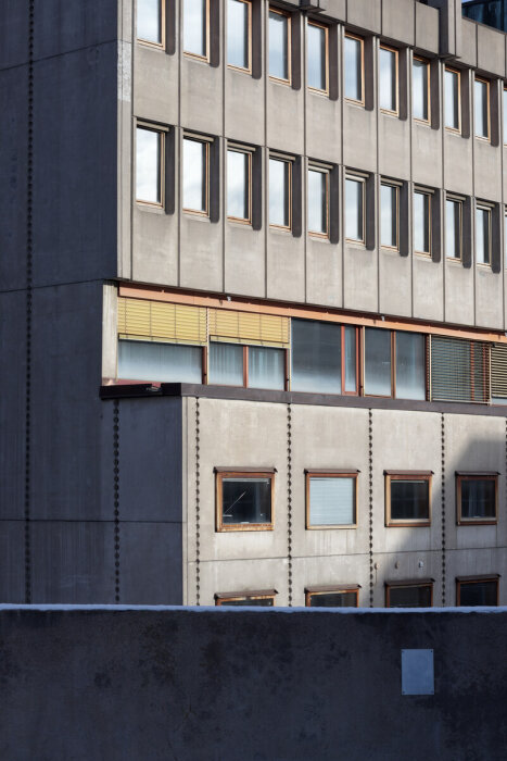 Fasad av betongbyggnad med rader av rektangulära fönster. Detaljerade kanter och skuggor syns på väggen.