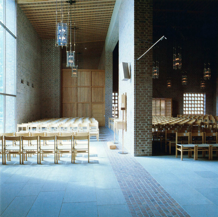 Interiör av Härlanda kyrka med tegelväggar, trästolar i rader och glashängande lampor, utformad av arkitekt Peter Celsing.