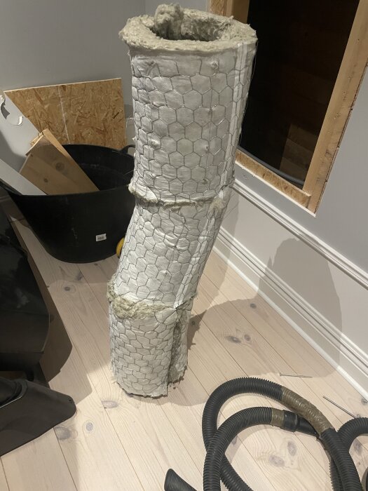 Imkanal med ljuddämpare i kattvind under renovering, stående på ljust trägolv bredvid verktyg och material.