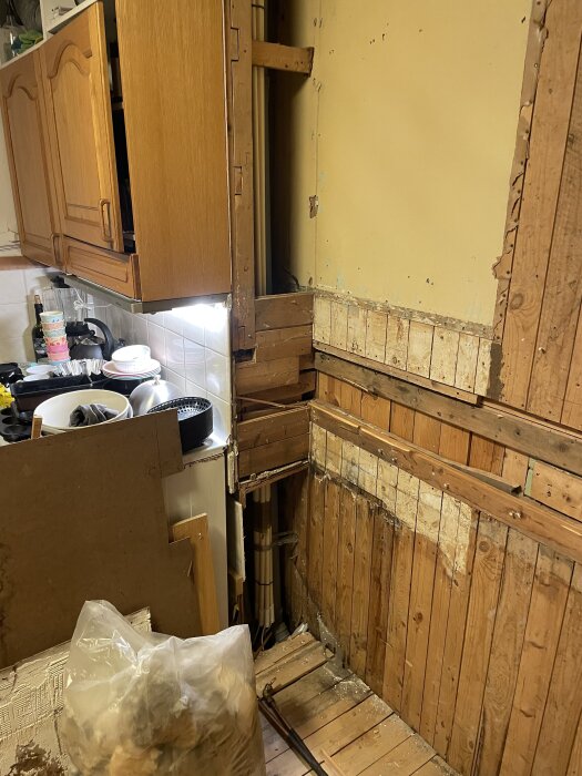 Delvis rivet kök med synliga träväggar och tak; gamla diskbänken borttagen. Verkar vara under renovering för att öppna upp mot skafferi.