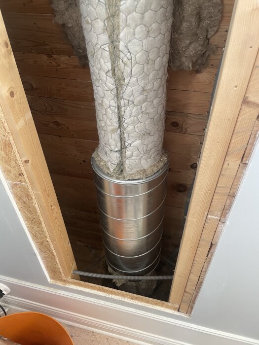 Vägg med utskuret hål och synlig imkanal täckt med isolering och galler, del av renoveringsarbete i köket.