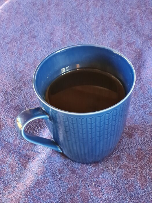 Blå mugg med te placerad på en lila texturerad duk.