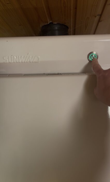 Hand trycker på en strömbrytare på en vit Sunwind-enhet, med ett grönt belyst på/av-symbol.