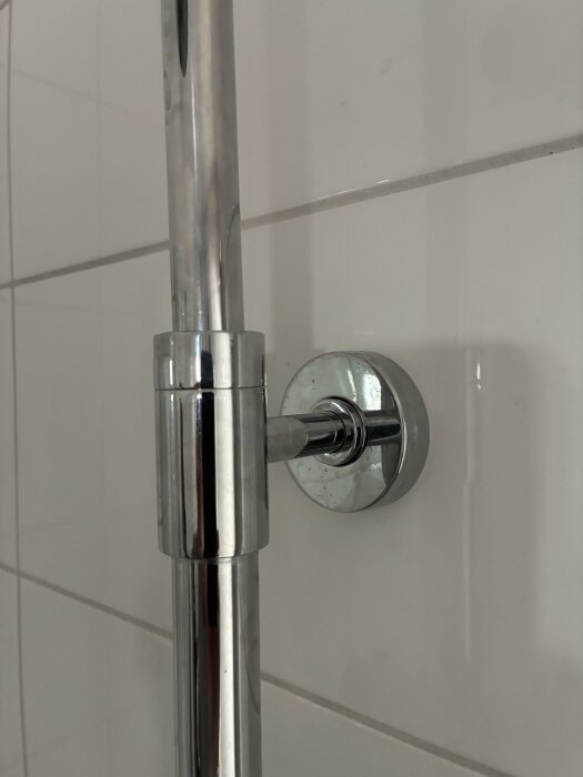 Kromad duschstång monterad på vitt, kaklat badrumsvägg.