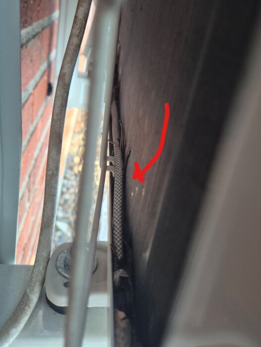 Kabel längs en vägg med en röd pil markerad ovanpå, invidligt exponerad och slarvigt placerad.