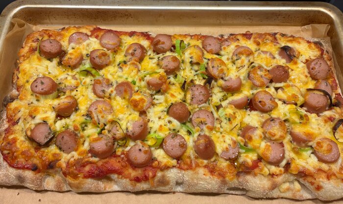 Pinsa toppad med skivad korv, purjolök och smält ost på en bakplåt, serverad igår med pepparsalami.