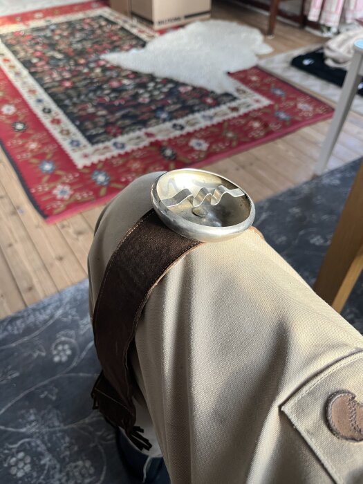 Portabel askkopp liggandes på ett knä i en sommarstuga med en orientmatta i bakgrunden.