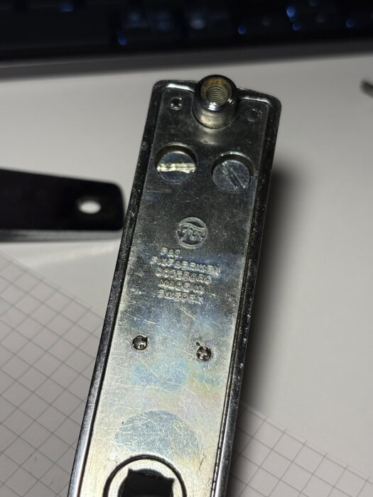 Bilden visar baksidan av ett metallhandtag från Fix Fabriken, med stämplat text och två skruvar.