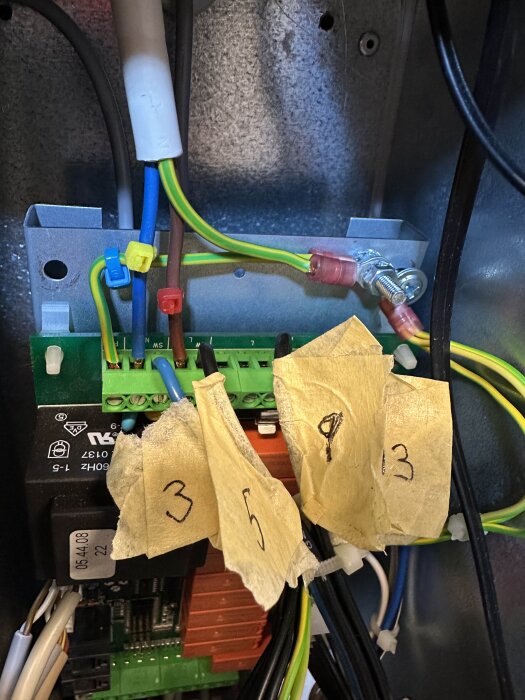 Elektriska kablar märkta med tejp i ett ventilationsaggregat, kopplade till ett grönt kretskort med olika färgade anslutningar.