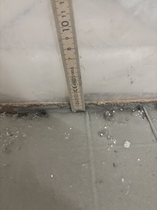 Ytans djup mäts med en linjal som visar ca 1 cm mellan armering och parkett i byggprojektet.