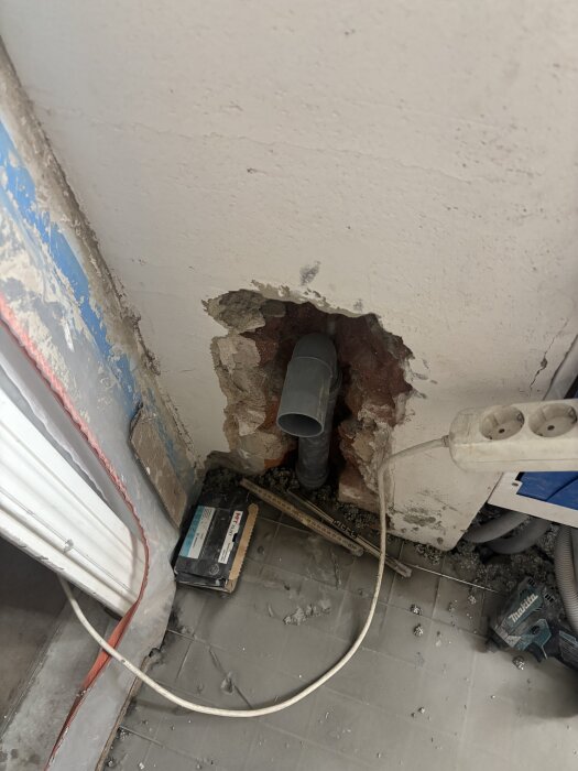 Skadat hål i väggen med ett grått rör och verktyg runt omkring. Fråga om säkerhet vid golvvärmeinstallation och avstånd till parkett.
