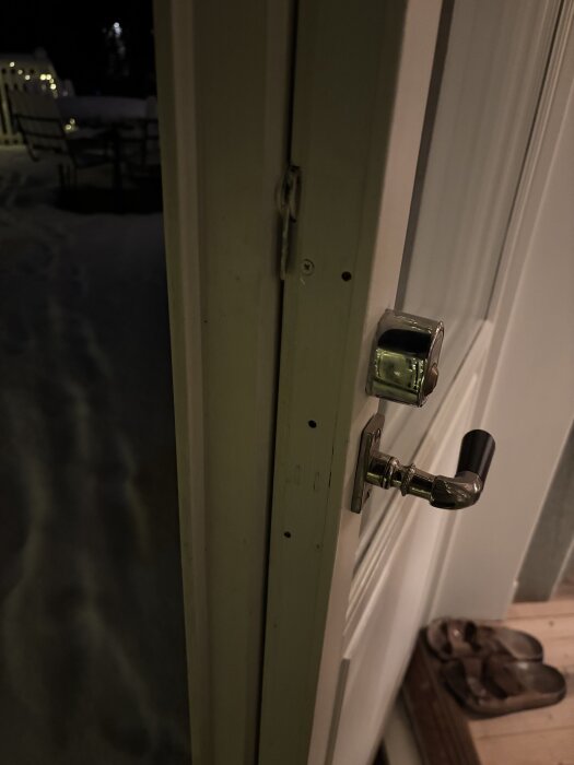 En dörr öppnas mot utsidan med synligt dörrhandtag och mörk vintermiljö utanför, med sandaler vid tröskeln.