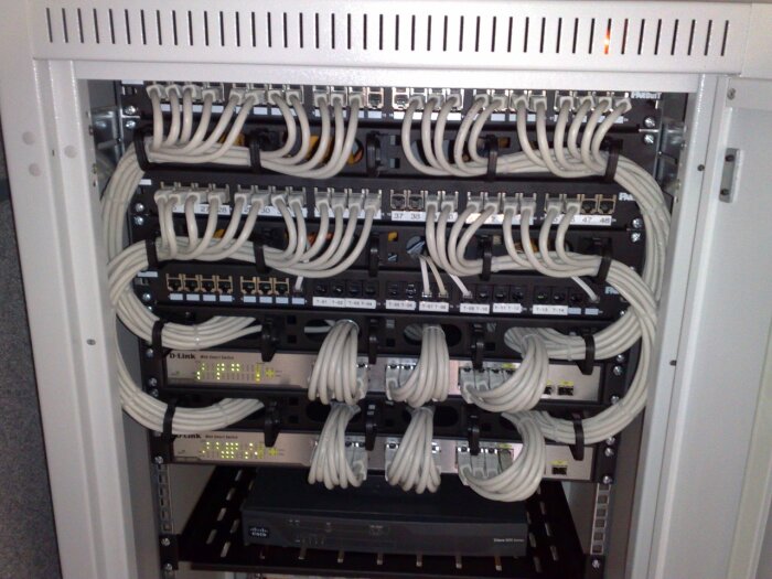 Stor patchpanel med kablar och switchar, synliga portar och etiketter. Kabelorganisation med buntband, tydlig nätverkskonfiguration.
