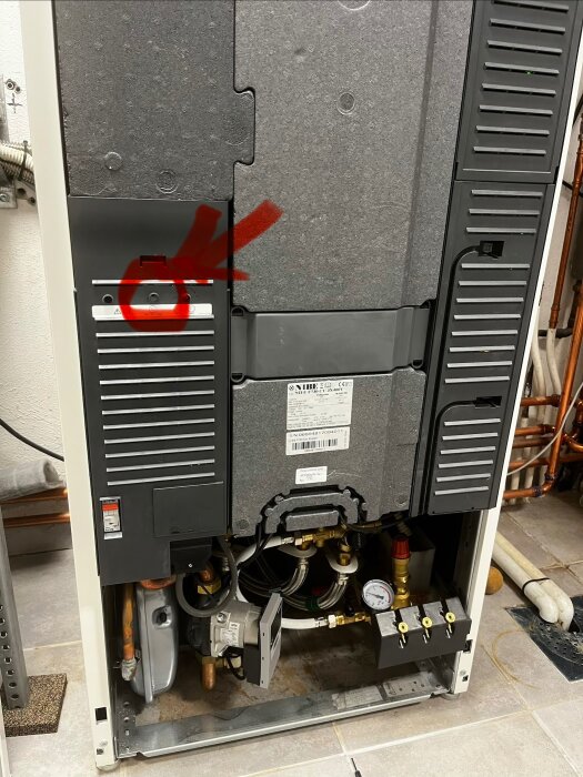 Värmepump med ett markerat område för återställningsknapp, omgiven av rör och ventiler, är det rätt plats att återställa larmet?