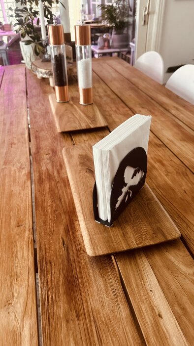 Ekbord med salt- och pepparkvarnar samt servetthållare på rektangulära serveringsunderlägg i trä.