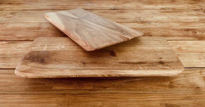 Två tjocka serveringsunderlägg i ek med mjuka former ligger på ett träbord.