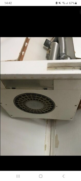 Fläktkåpa underifrån med fläktgaller, synliga ventilationsrör och inlägg om att byta lampa och justera plastpiggar för att lossa locket.