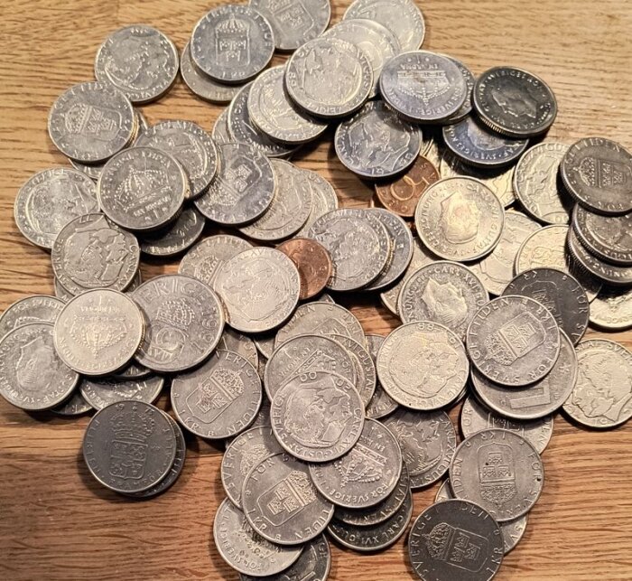 En hög med svenska mynt, inklusive enkronor, femkronor och femtioöringar, på ett träbord.