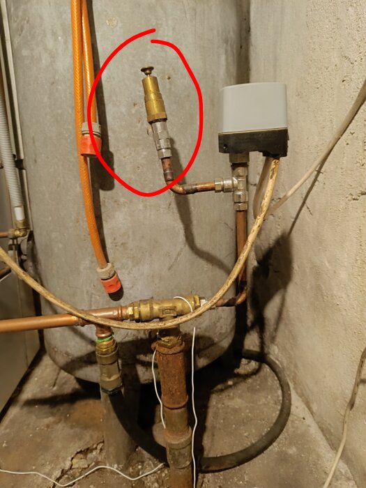 Vattenrör med tryckbrytare och ventil markerad med röd cirkel, okänd komponent efter tryckbrytaren i ett rum med betongväggar.